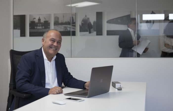intervista a claudio azzalin ritratto seduto sulla sua scrivania in Movinlog ripreso a tre quarti sorridente in piano americano