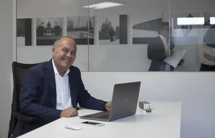 intervista a claudio azzalin ritratto seduto sulla sua scrivania in Movinlog ripreso a tre quarti sorridente in piano americano