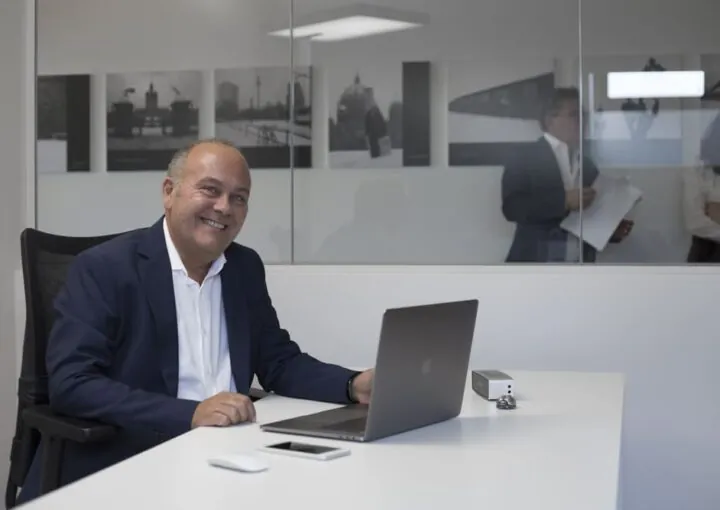 intervista a claudio azzalin ritratto seduto sulla sua scrivania in Movinlog ripreso a tre quarti sorridente in piano americano