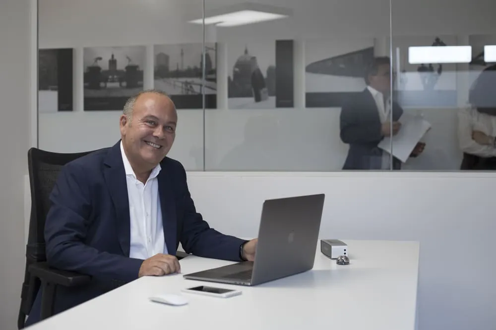 intervista a claudio azzalin ritratto seduto sulla sua scrivania in Movinlog ripreso a tre quarti sorridente in piano americano